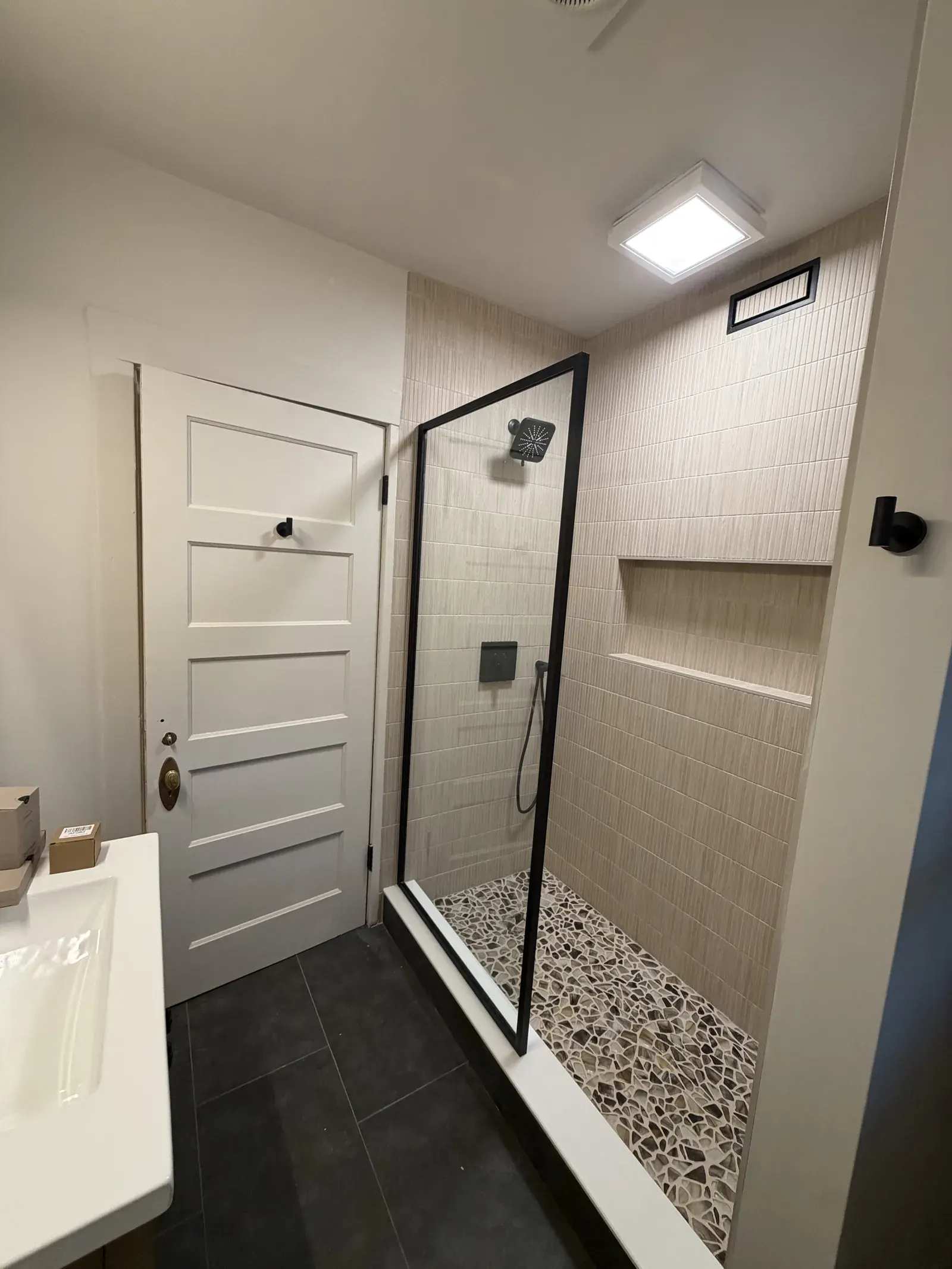 Walk-in shower — framed glass, pebble-stone pan, ceramic surround with niche